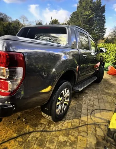 Black pickup truck being washed on a driveway during an exterior detail