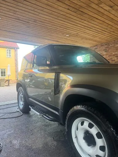 Dark green Land Rover Defender under a carport after an exterior detail