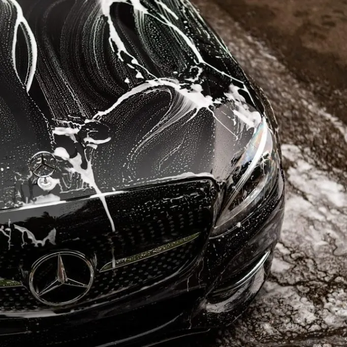 Black Mercedes covered in snow foam during the pre-wash stage of an exterior detail